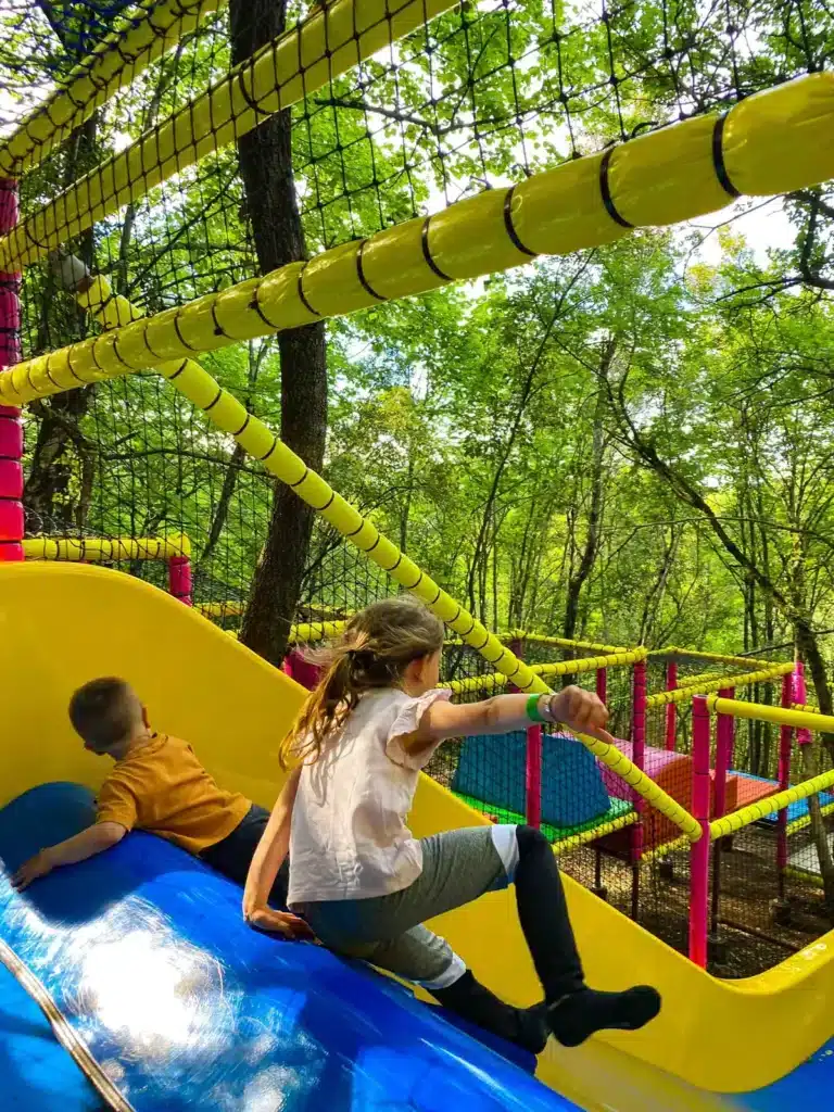 Enfants s’amusant sur un toboggan coloré dans une zone de jeux sécurisée du Parc Casse-Noisette, un parc d’attraction en pleine nature.